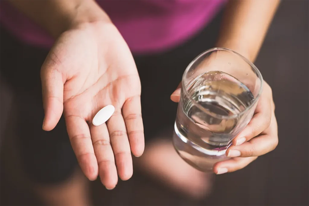 person with glass of water and pill in hand